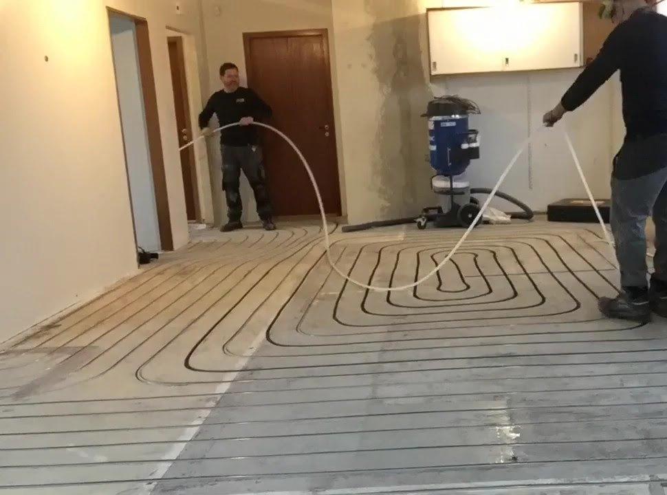 Tveir starfsmenn leggja gólfhitarör í fræstar rásir