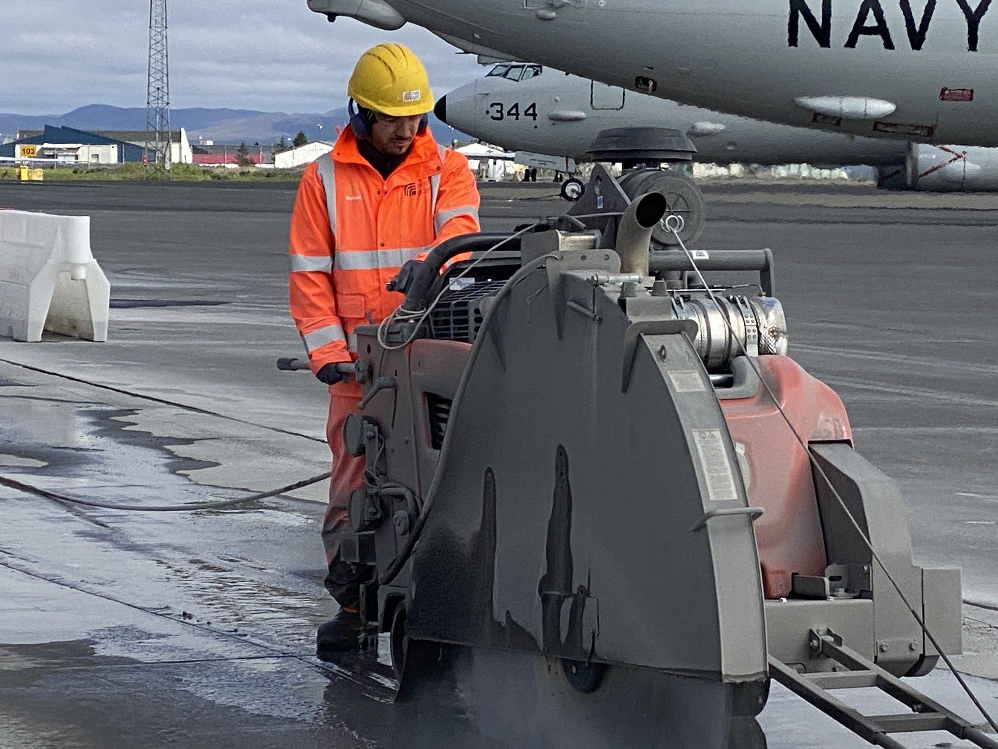 Starfsmaður sagar steinsteypu með stórri sög á flugvelli